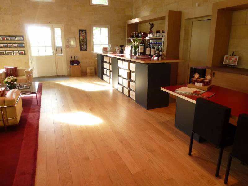 Spacieux magasin de vins avec comptoir de dégustation, bouteilles, sol en bois clair, mobilier d'accueil et lumière naturelle.