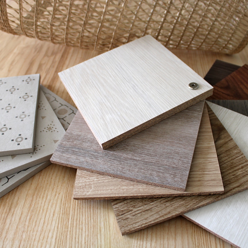 Échantillons de matériaux : bois, carrelage texturé et motifs géométriques, posés sur du bois clair avec panier en osier en fond.