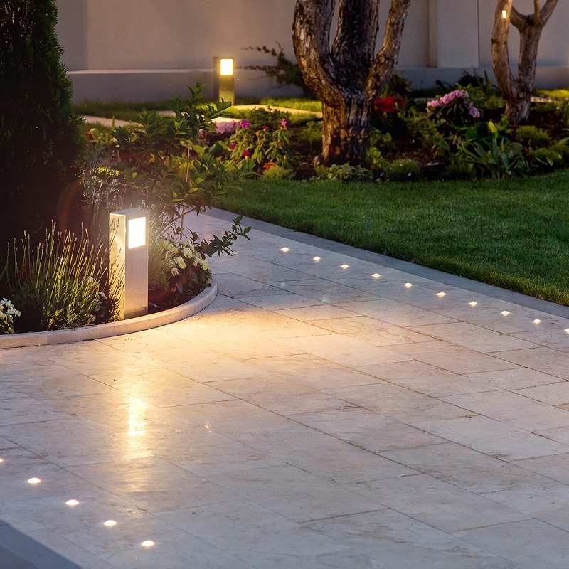 Chemin de jardin pavé éclairé par des lumières encastrées et un lampadaire la nuit, ambiance douce et sécurisée.