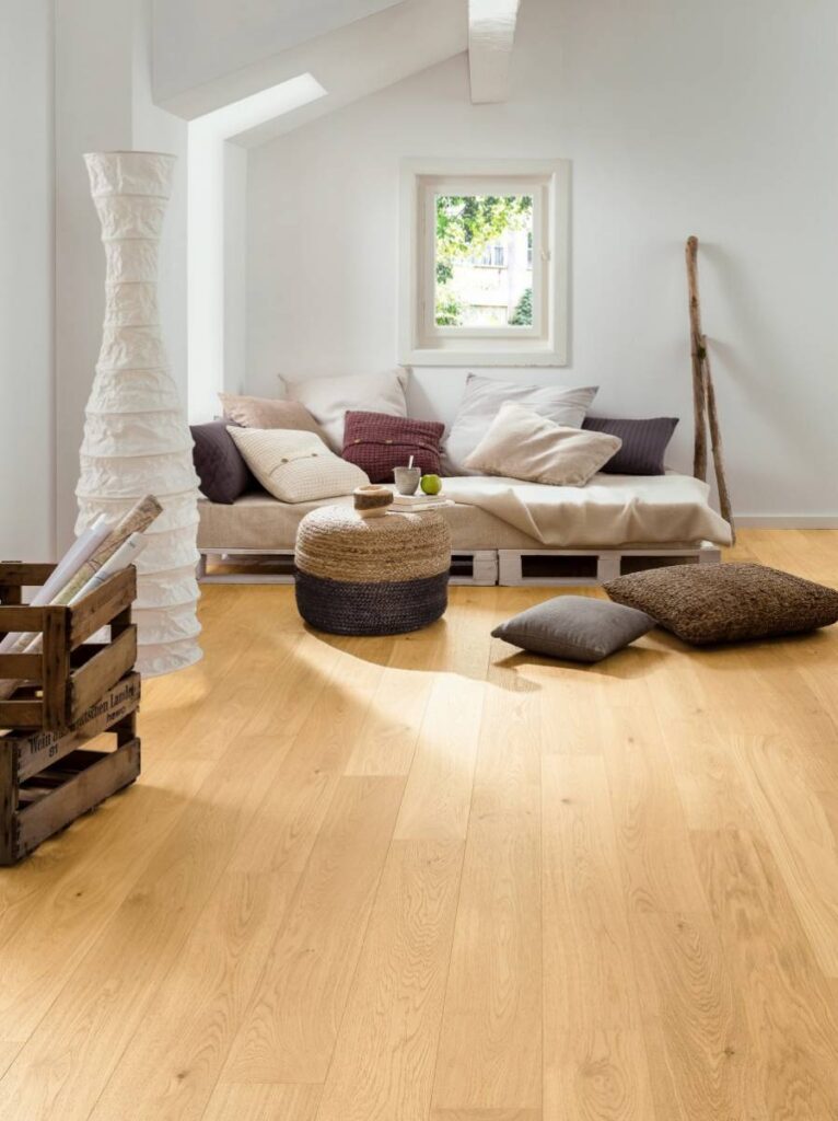 Salon lumineux : parquet clair, canapé palettes et déco Salon lumineux avec parquet clair et canapé palettes. Coussins, pouf tressé, lampe papier et caisse "Wein aus deutschen Landen" en bois.